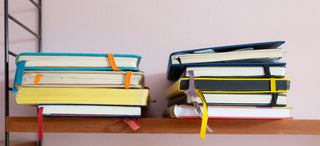 zwei Stapel mit gebrauchten Notizbüchern in verschiedenen Farben und Größen in einem Bücherregal