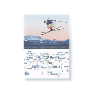 Ein Skifahrer schwebt in der Luft über einem winterlich verschneiten Dorf mit Bergen im Hintergrund.