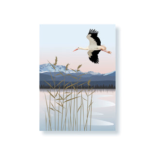 Ein Storch fliegt über einen See mit Schilfgras und verschneiten Bergen im Hintergrund